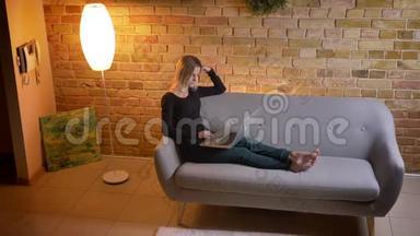 在舒适的室内沙发上坐着，年轻漂亮的女青少年在笔记本电脑上上网的侧景肖像。